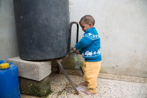 A young child in Gaza gets water from a holding tank at their home.